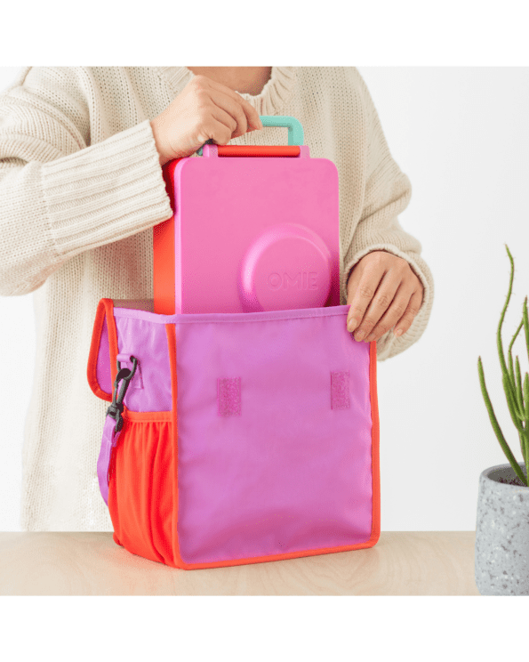 foldable lunch bag with pockets and strap by OMIE in pink color holds the OMIE Box, OMIE Box Up, OMIE dip & Omie Pod, water bottle and cutlery!